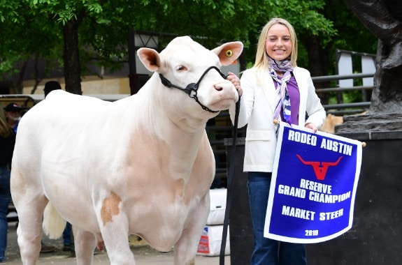 A young woman holding an award banner standing next to a white steer.