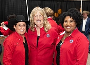 A group of three volunteers wearing red Rodeo Austin jackets standing next to each other.